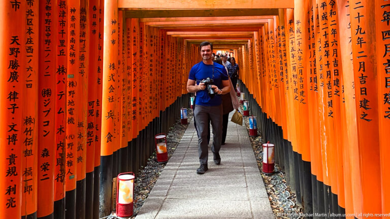 Photographer posing with a camera inside a corridor of vermilion torii.