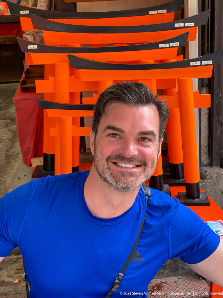 Smiling visitor beside a display of miniature vermilion torii.