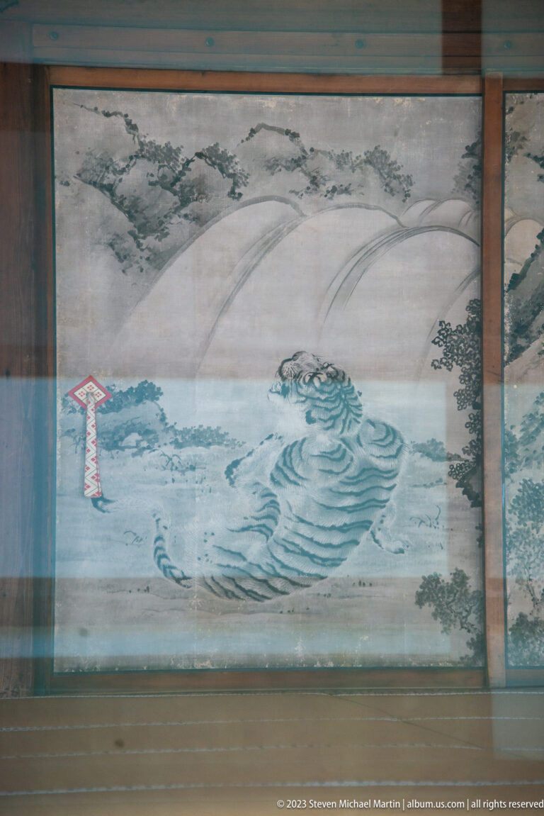 Blue-green waves and a pale landscape painted across sliding palace panels behind glass.