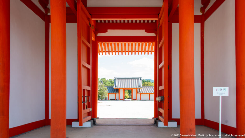Axial view through a vermilion gate toward a smaller red gateway across the courtyard.
