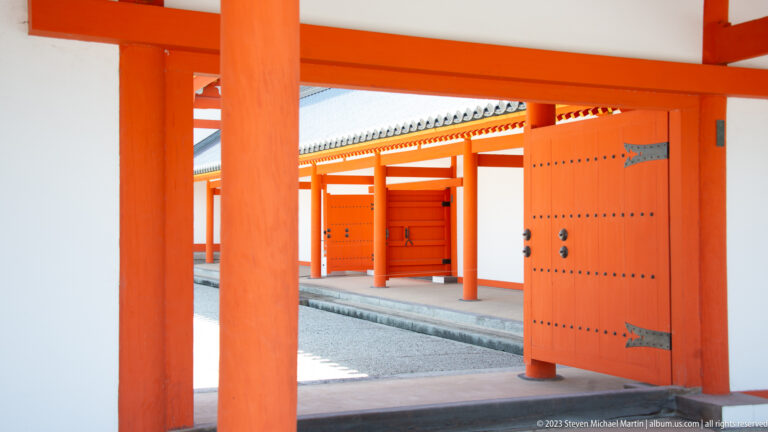 Vermilion colonnade with white wall panels and a large open studded door.