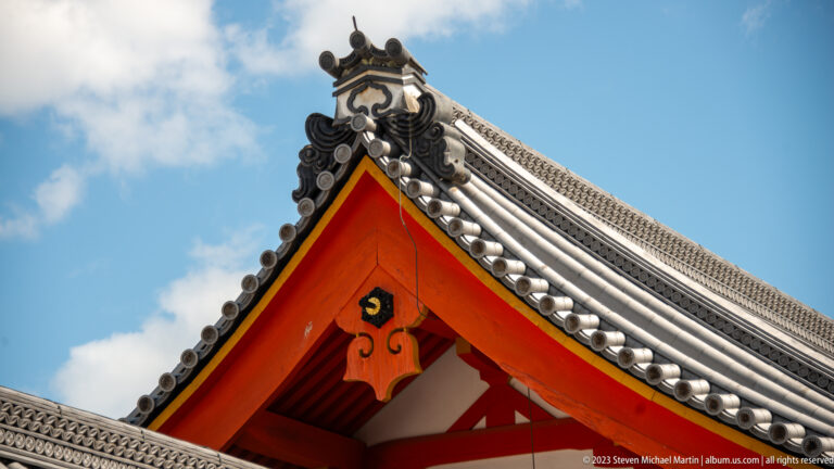 Steep palace gable with gray roof tiles, ridge ornaments, and a small central emblem.