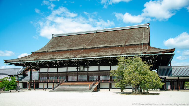 Large traditional palace hall with broad brown roof, raised floor, and central steps.