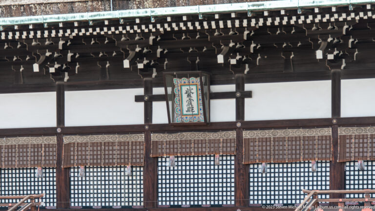 Calligraphic plaque centered beneath deep timber eaves on a palace hall façade.