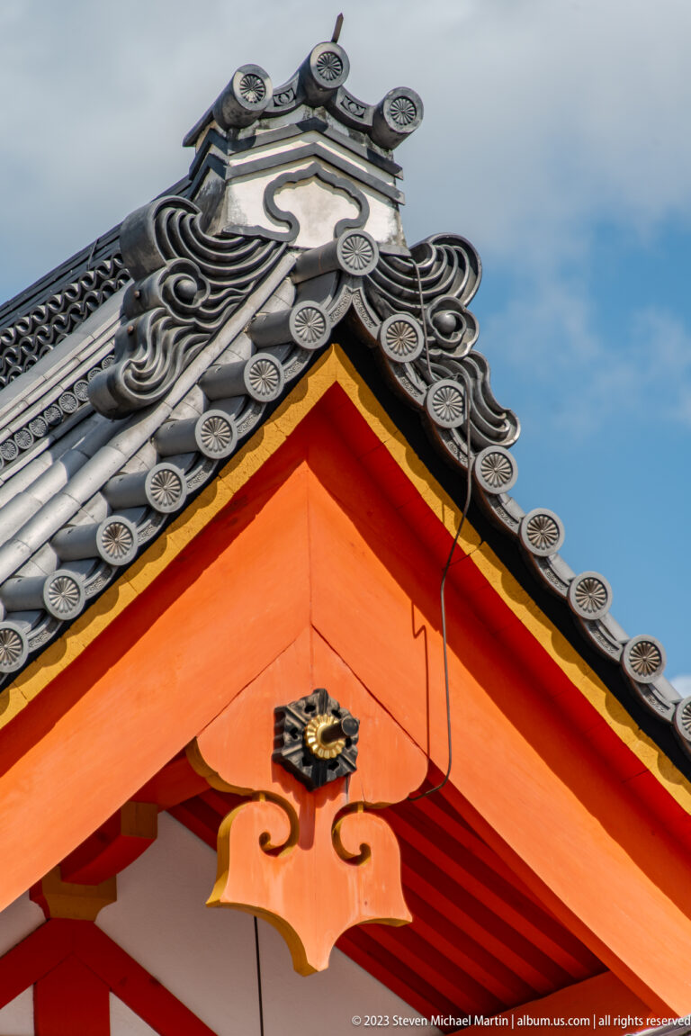 Close-up of gray ridge tiles and ornamental motifs above a vermilion palace gable.