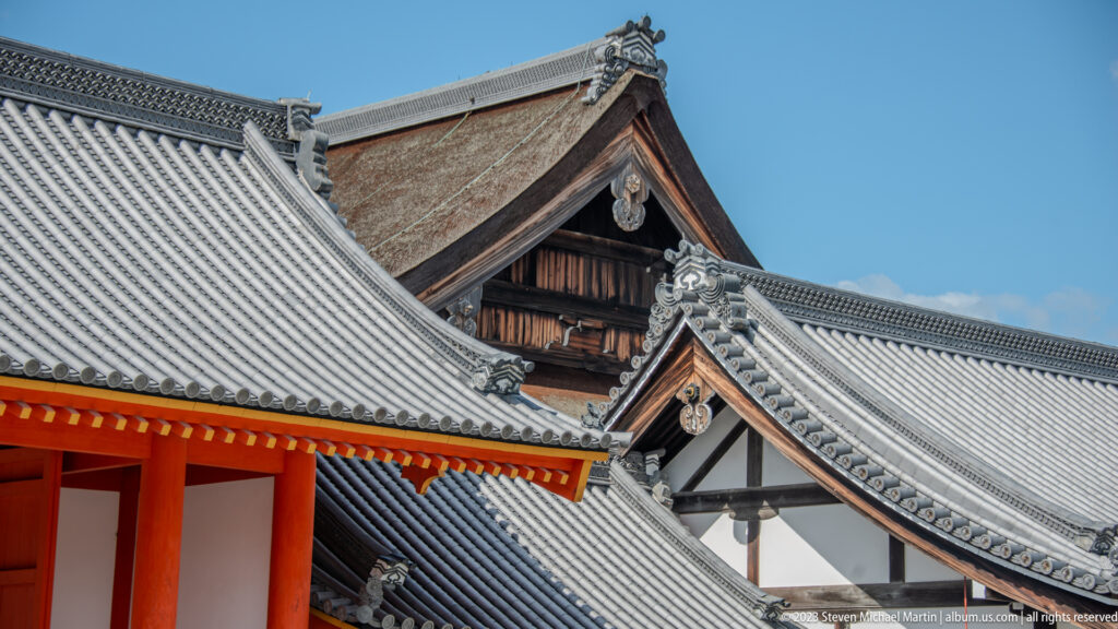 Layered palace roofs and gables with gray tiles, dark timber, and vermilion supports.