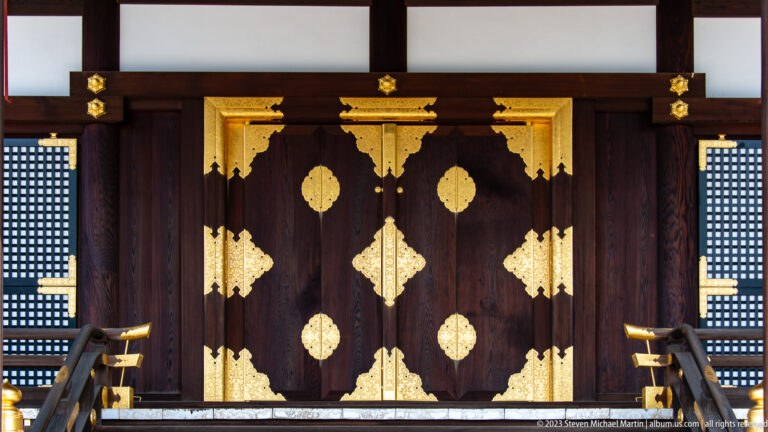 Dark wooden palace doors covered with symmetrical gold decorative fittings.