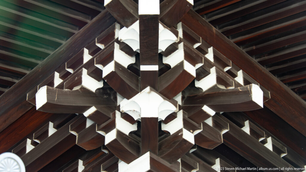 Symmetrical close-up of interlocking dark timber brackets with white-painted ends.