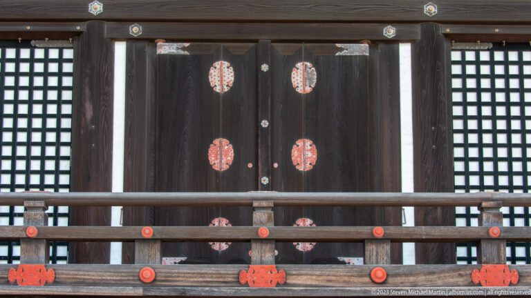Dark timber palace doors and lattice windows with repeated red metal fittings.