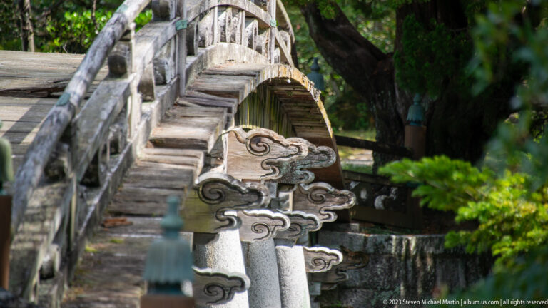 Close detail of a weathered garden bridge with carved cloud-shaped support.
