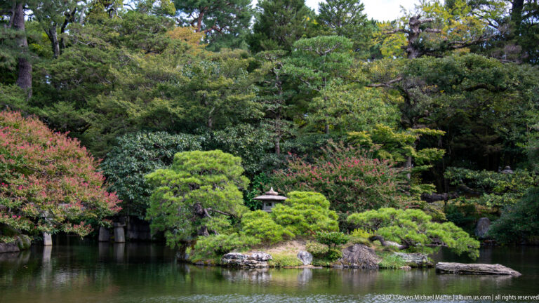 Palace garden pond bordered by clipped shrubs, rocks, trees, and a stone lantern.