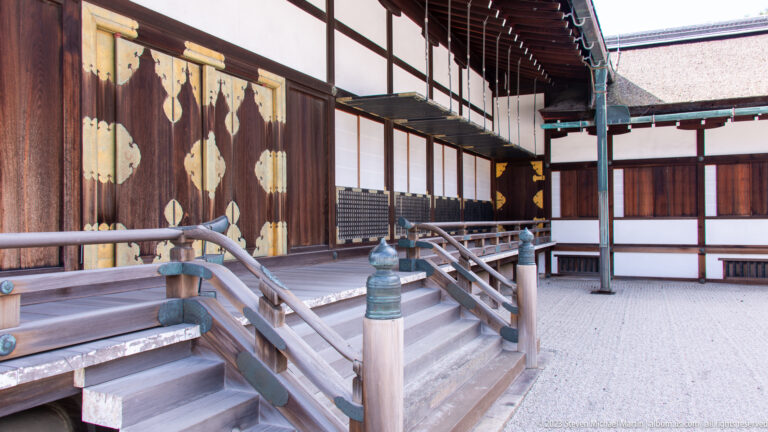 Raised palace veranda with shallow stairs, railings, and gold-fitted wooden doors.