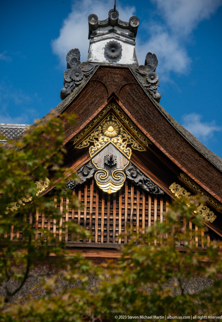 Ornate palace gable with gold decoration and crest seen through blurred foliage.
