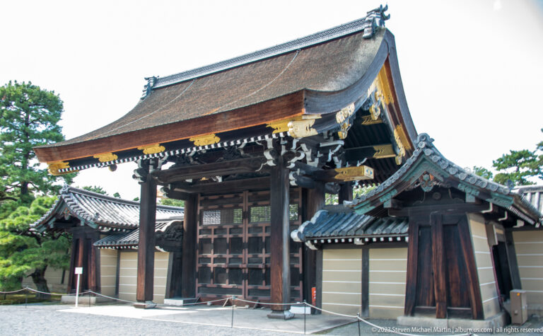 Oblique view of an ornate wooden palace gate with layered eaves and adjoining roofs.