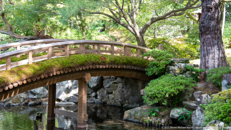 Small moss-covered arched wooden bridge over a narrow garden stream.