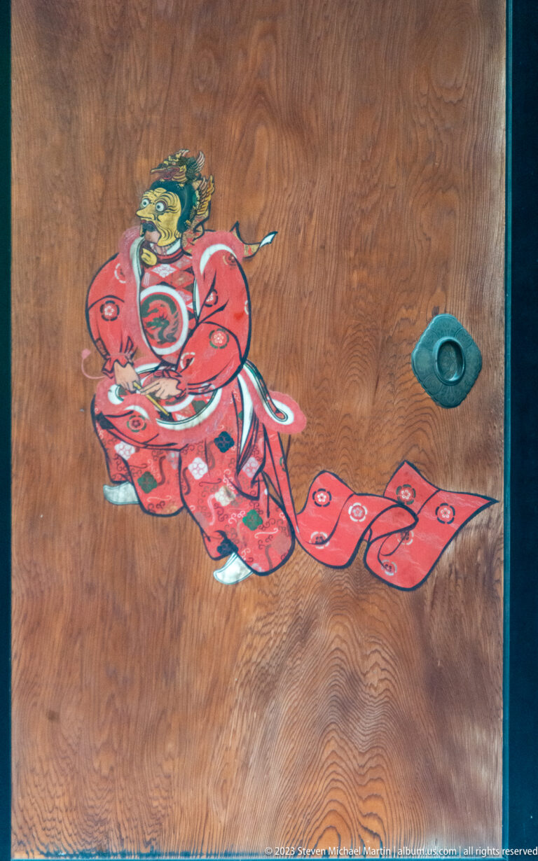 Colorful red-robed figure painted on a wooden panel beside a round metal pull.