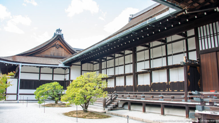 Palace courtyard bordered by timber buildings, verandas, and a prominent gabled roof.