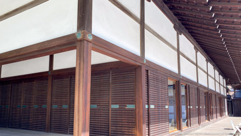 Long timber palace façade with white upper panels and rows of closed slatted shutters.