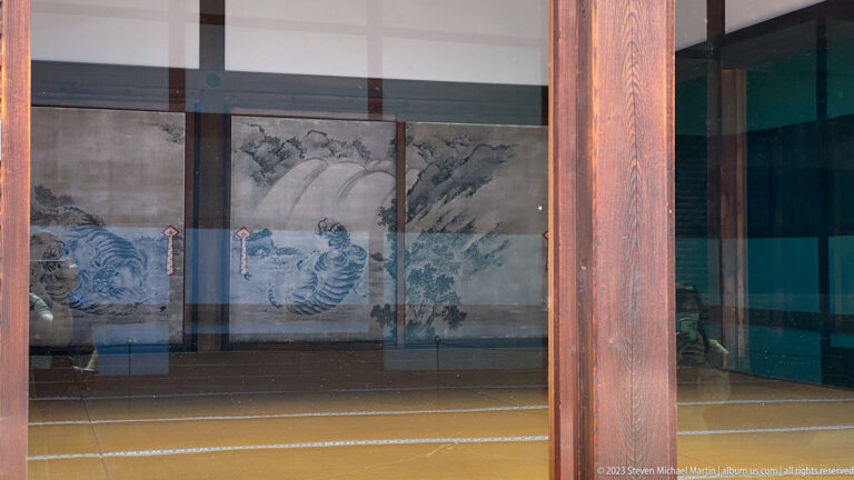 Monochrome waves, rocks, and trees painted across sliding panels in a tatami room.