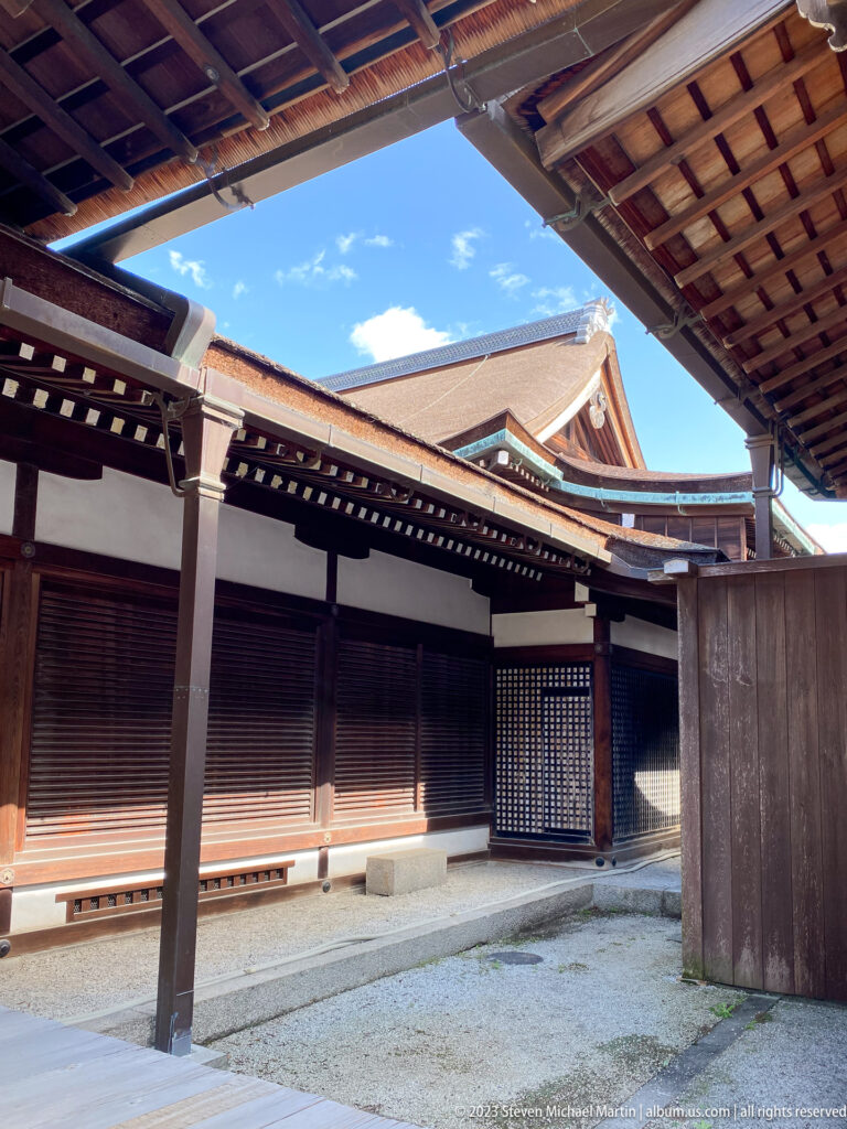 Wide gravel courtyard bordered by timber palace buildings, verandas, and trees.