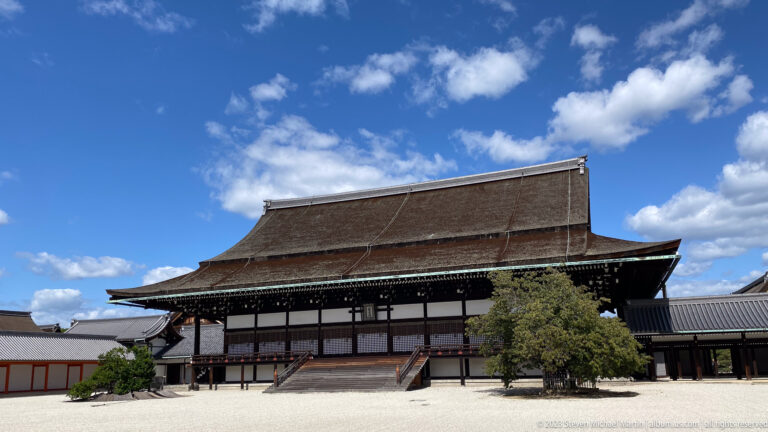 Large closed timber palace gate with deep eaves, tiled roof, and flanking trees.