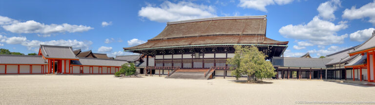 Panoramic palace courtyard with multiple traditional buildings and open gravel space.