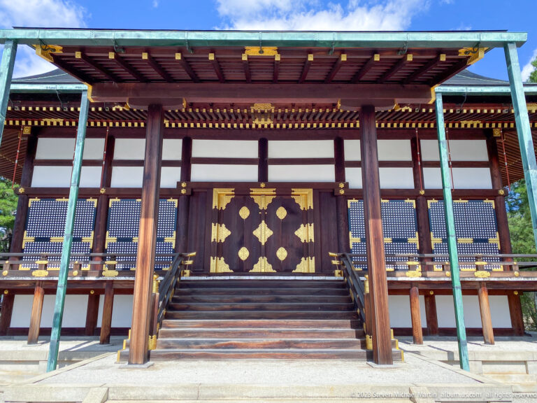 Large raised timber hall with broad roof, deep eaves, and central stairs.
