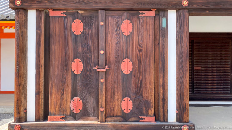 Large dark wooden double doors with repeated gold decorative fittings.