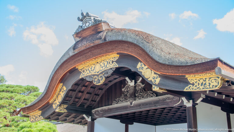 Close view of a curved palace-gate gable with gold ornament and dark timber latticework.