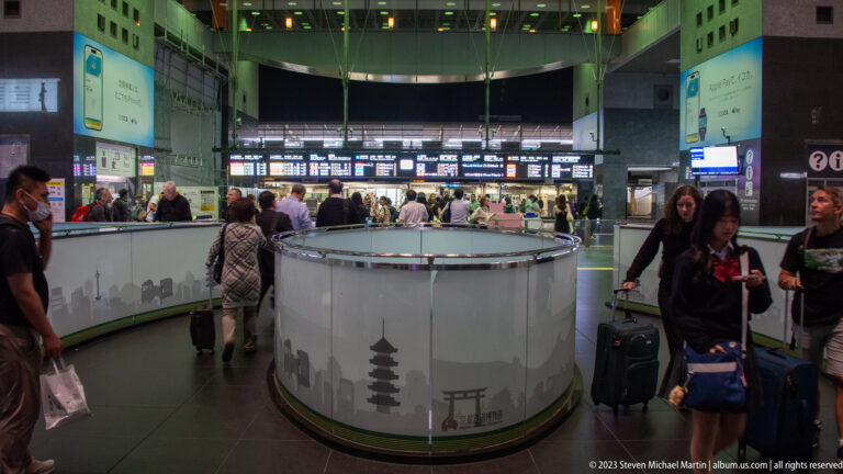 Circular station service counter decorated with Kyoto landmark silhouettes, with travelers and departure boards behind.