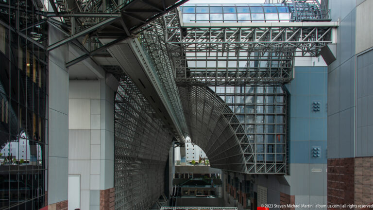 Vertical exterior view of Kyoto Station steel trusses, glazed bridges, and circulation structures between tall walls.