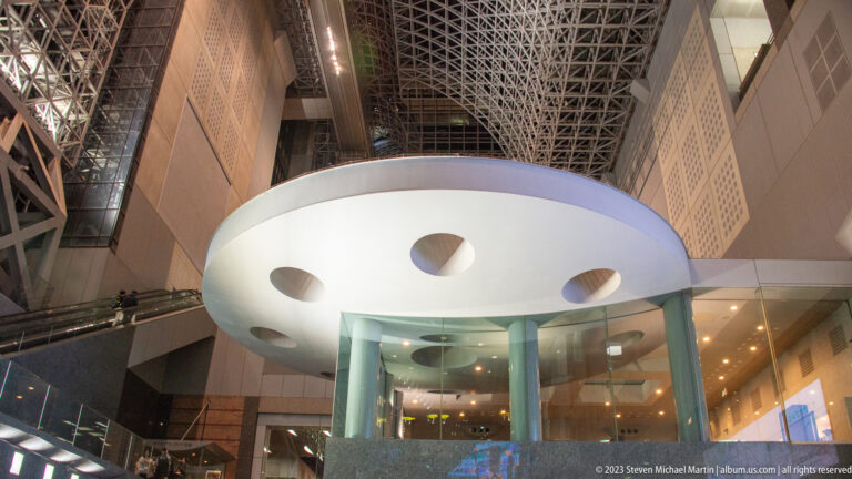 White circular canopy with oval openings and glass supports inside Kyoto Station's atrium.