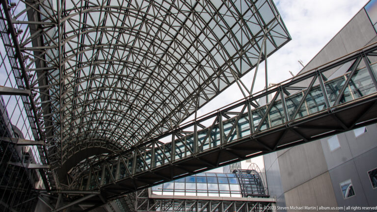 Glass-enclosed pedestrian bridge crossing beneath Kyoto Station's curving steel-and-glass roof.