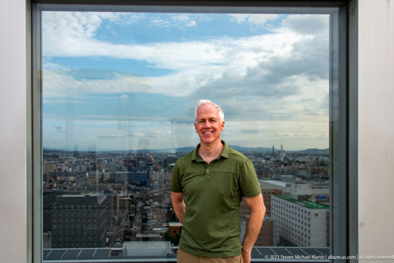Male visitor in a green shirt standing before a large window overlooking Kyoto.