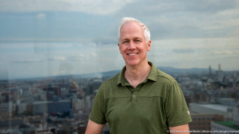 Close portrait of a smiling male visitor in a green shirt with Kyoto softly blurred behind him.