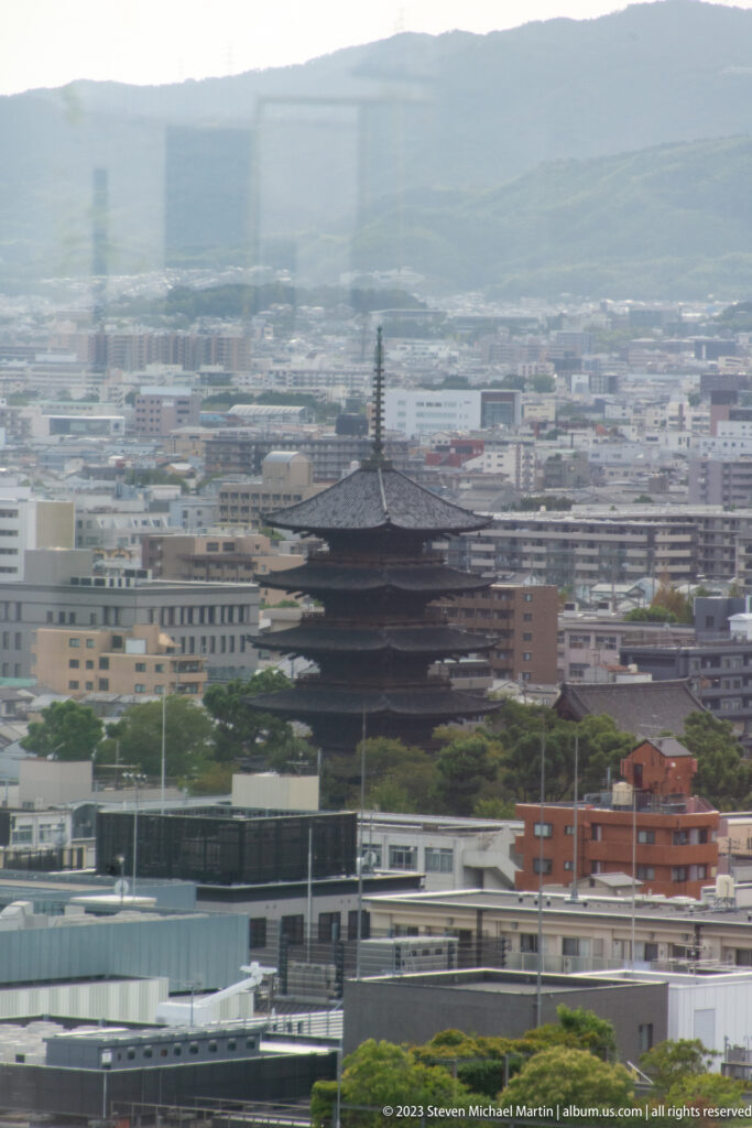 Distant view of Tō-ji's five-story pagoda above Kyoto rooftops with hazy mountains beyond.