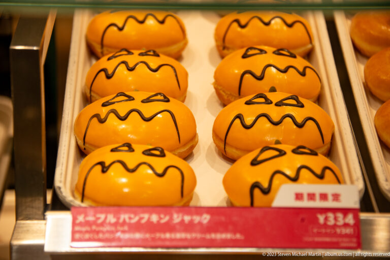Rows of orange glazed character-themed doughnuts displayed in a bakery case with price labels.