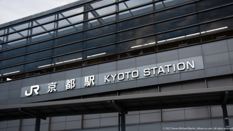 Close view of JR Kyoto Station exterior sign beneath dark glass facade.