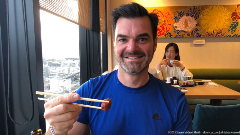 Visitor holding chopsticks during a meal beside a window overlooking Kyoto.