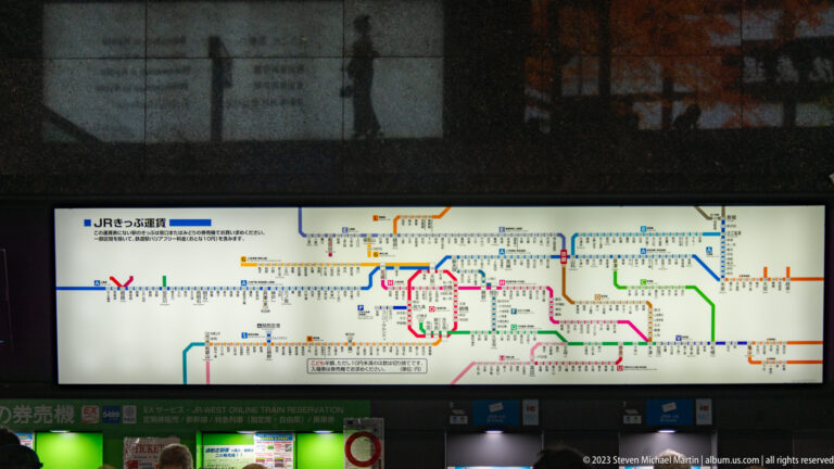 Illuminated JR West railway network map with colored routes above ticketing equipment in Kyoto Station.