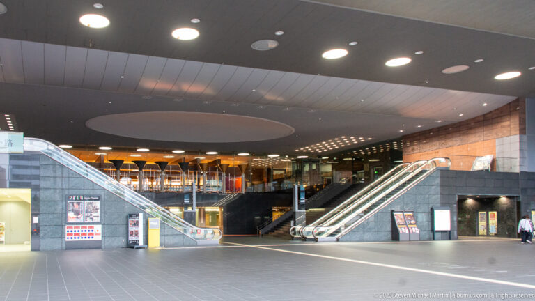 Wide station concourse with paired escalators and open floor.