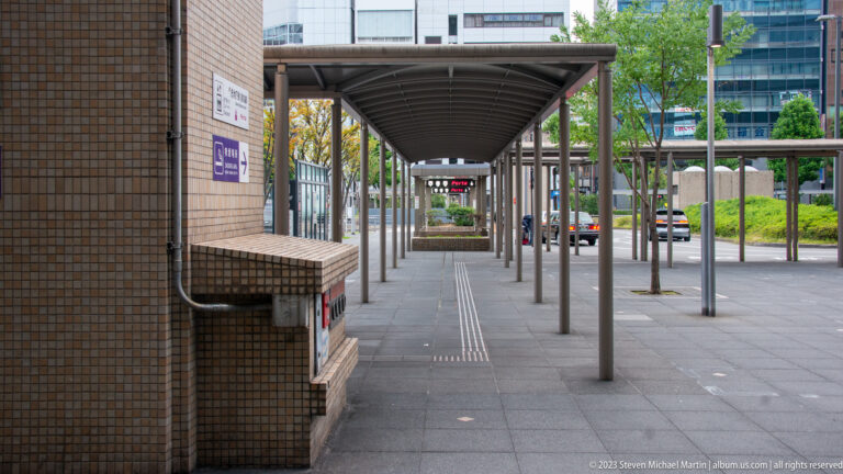 Covered pedestrian walkway with repeating columns and tactile paving.
