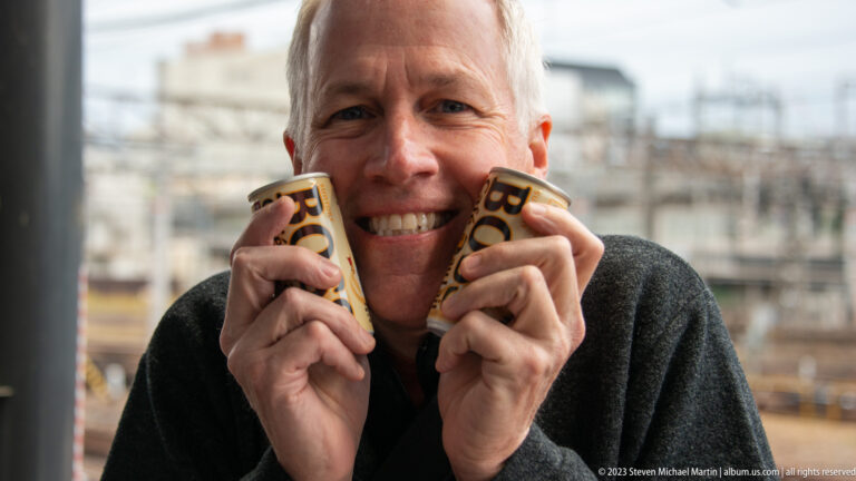 Smiling visitor holding two canned coffee drinks.