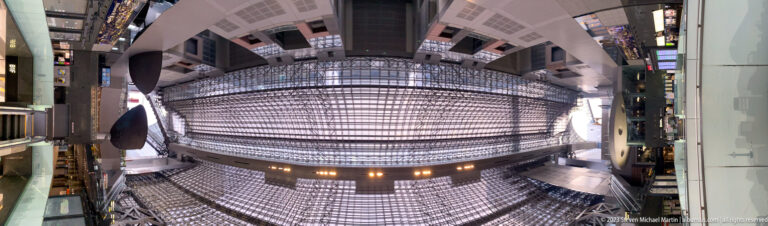 Upward fisheye view of Kyoto Station's curved steel lattice roof and surrounding upper-level openings.