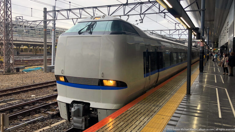Limited Express train standing at a Kyoto Station platform beside tactile paving and overhead railway infrastructure.
