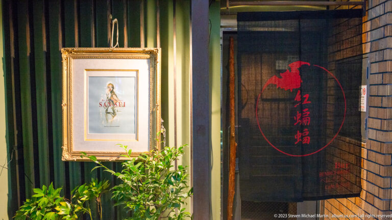 Artistic storefront with framed illustration and Japanese signage shown at night with the principal architectural, landscape, or street details visible in the composition.