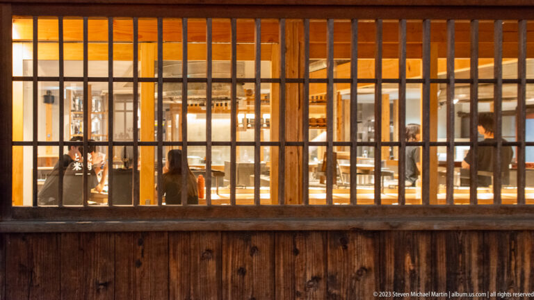 Dining room viewed through machiya lattice façade shown at night with the principal architectural, landscape, or street details visible in the composition.