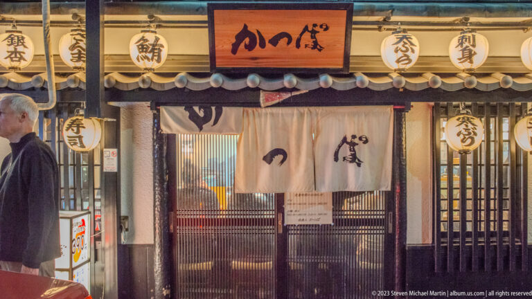 Traditional Kyoto restaurant with tiled eaves, paper lanterns, wooden latticework, and pale noren curtains.