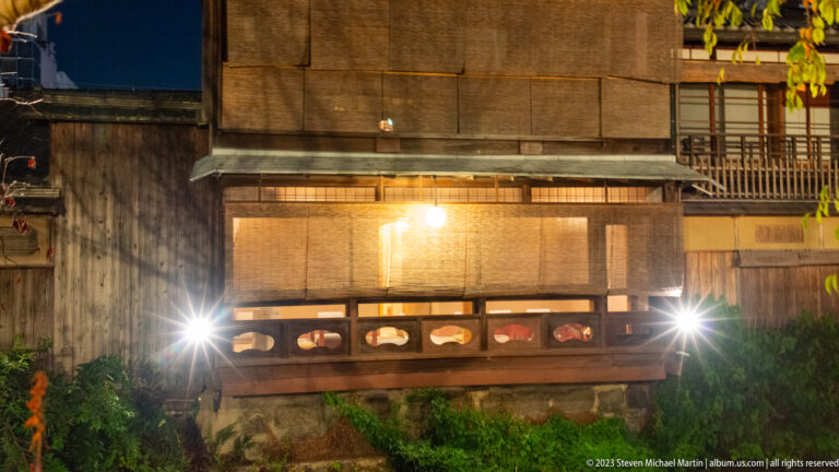 Canal-side machiya façade with bamboo blinds shown at night with the principal architectural, landscape, or street details visible in the composition.