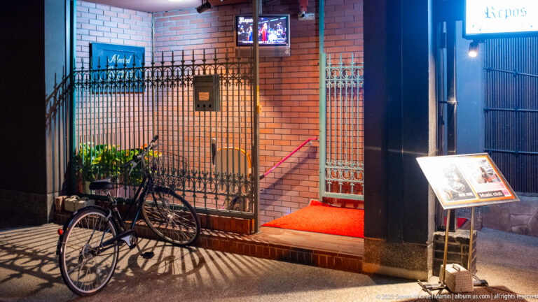 Urban entrance with bicycle and menu stand shown at night with the principal architectural, landscape, or street details visible in the composition.